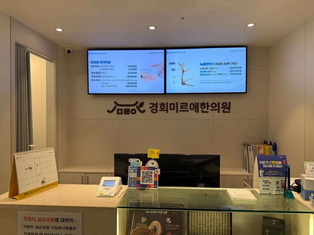 한의원 접수대 상단에 설치된 디지털 사이니지 — 면역약침·녹용한약 가격과 진료 정보를 안내하는 실제 운영 화면